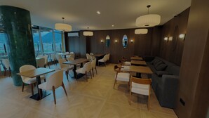 A modern restaurant with a mix of tables and seating areas, large windows offering a view, and contemporary lighting fixtures.