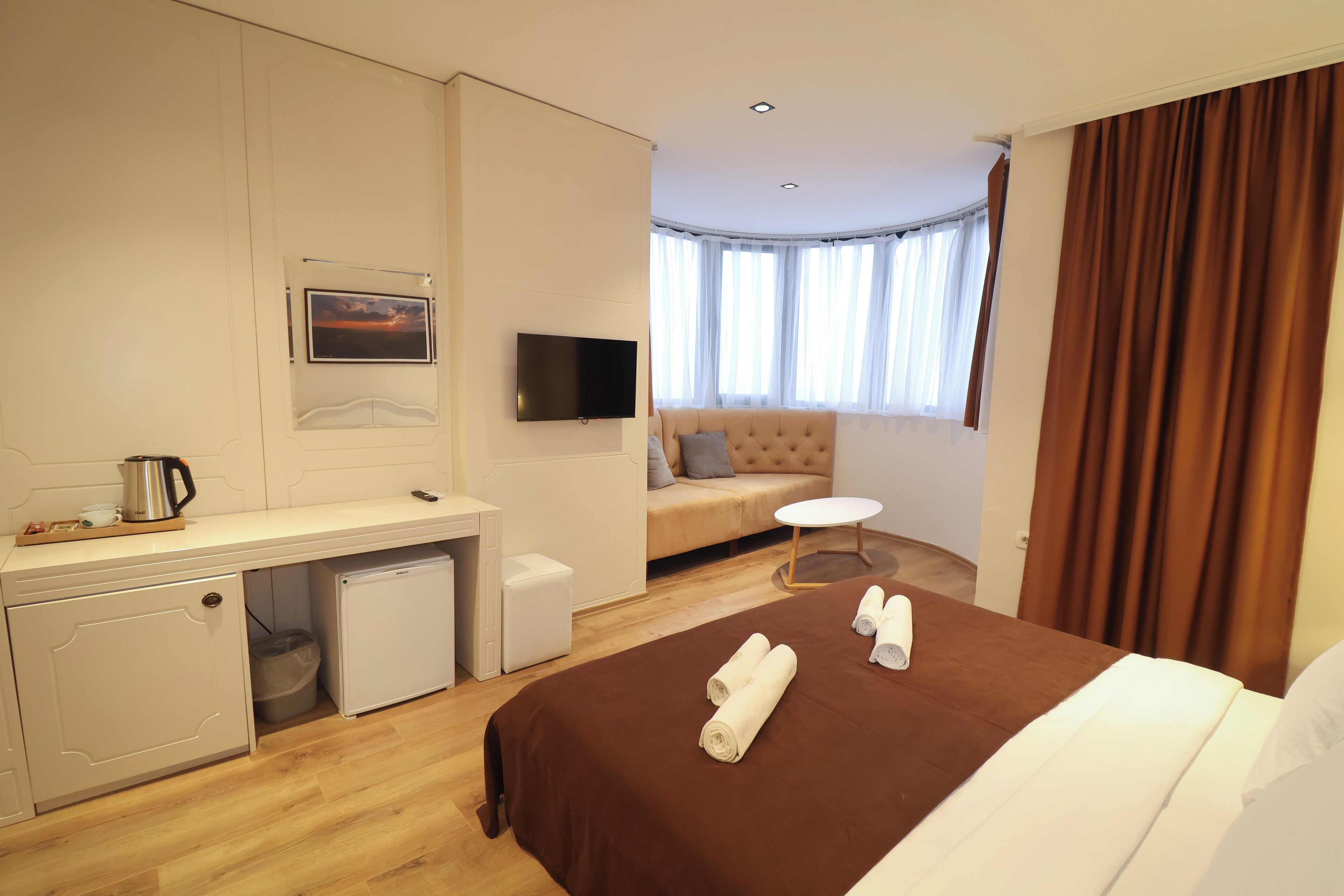 A hotel room with a bed, a desk, a small refrigerator, a TV, and a window with curtains.