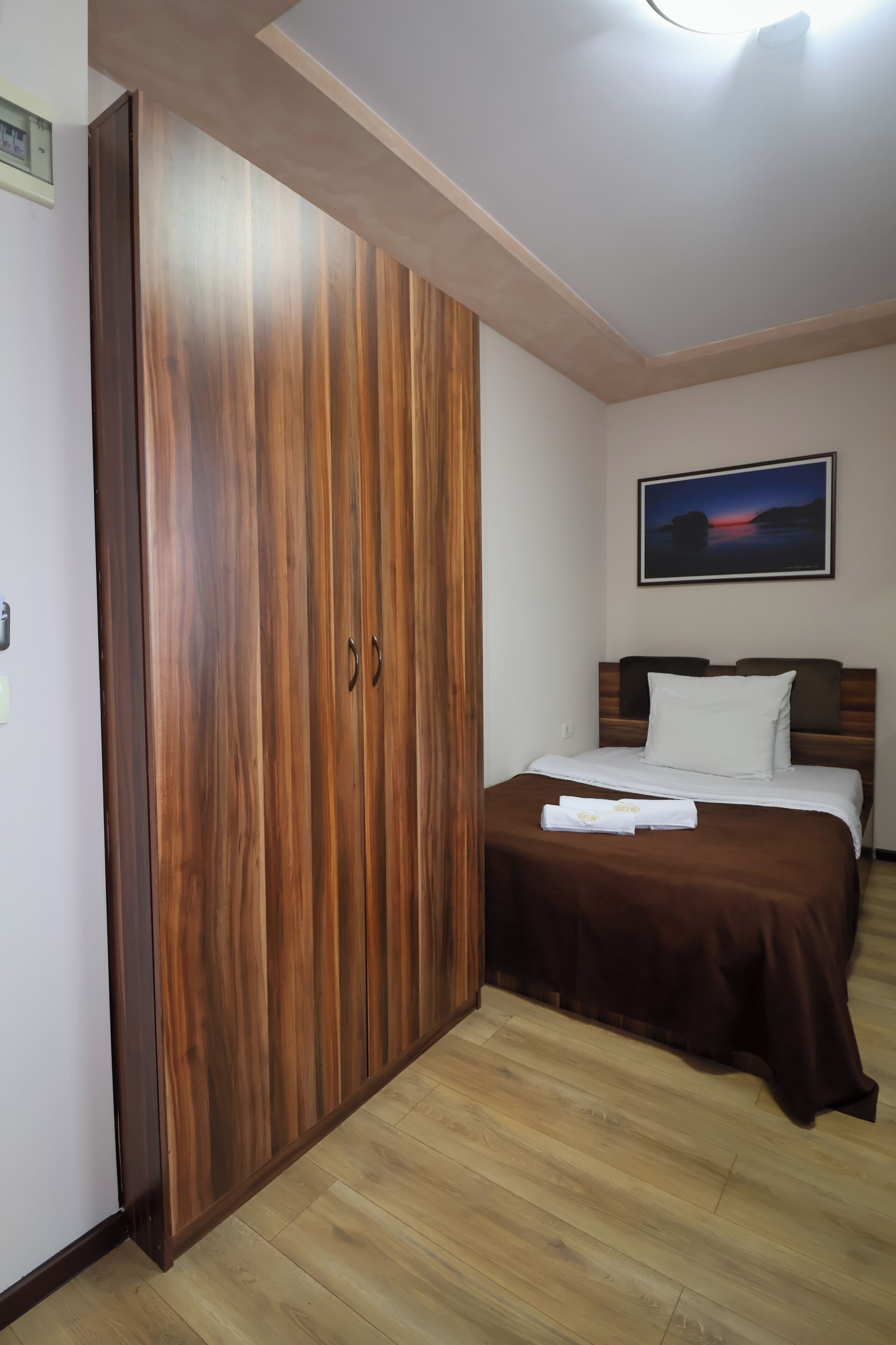 Une chambre à coucher avec une armoire en bois, un lit recouvert d’une couverture marron et un tableau encadré accroché au mur.