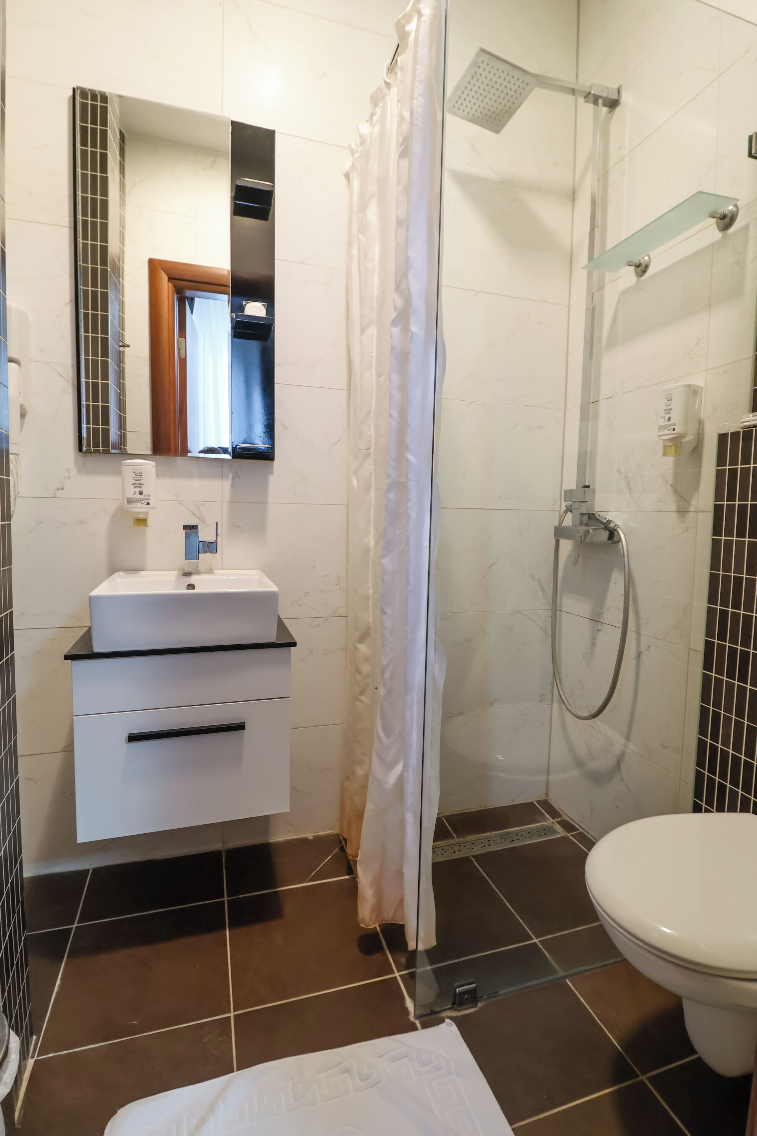 A bathroom with a white sink, a mirror, a shower, and a toilet.
