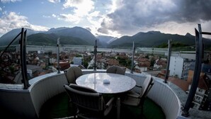 A round table with chairs on a balcony overlooking a town and mountains.