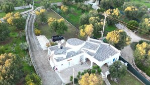 An aerial view of a white building with a curved roof, surrounded by greenery and a winding road.