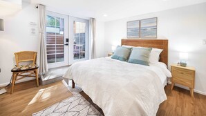Slaapkamer met een groot bed, een houten nachtkastje, een rieten fauteuil en uitzicht door een schuifdeur.