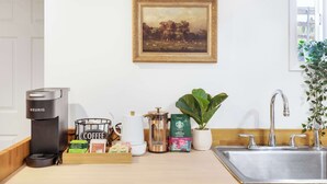 Een moderne keuken met een Keurig koffiezetapparaat, een koffiemolen, een gootsteen en een schilderij van een landschap aan de muur.