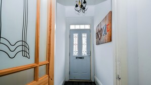 Un couloir avec une porte en bois, un lustre et un mur orné d’un panneau sur lequel est écrit le mot « AMOUR ».