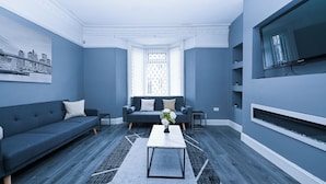 Un salon moderne avec un canapé bleu foncé, une table basse blanche et un grand téléviseur à écran plat fixé au mur.