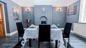 Un coin repas avec une table dressée pour quatre personnes, une horloge au mur et une cheminée.
