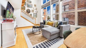 A modern living room with a grey sofa, a wooden dining table, and a staircase leading to another level.