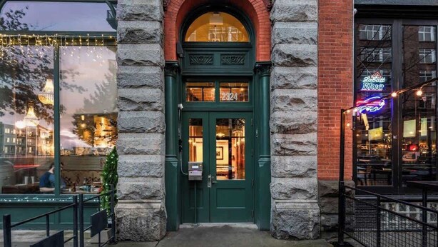 A brick building with a green door and a neon sign.