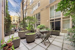 A courtyard with outdoor seating, potted plants, and a building with large windows. - Historic DT Loft w/ 16ft Ceilings, Garage &97 WS! (Seattle)