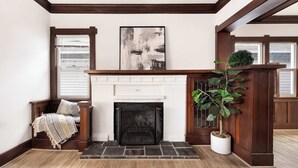 Habitación de esquina con chimenea, un banco con manta, una planta en maceta y una obra de arte abstracta enmarcada en la pared.