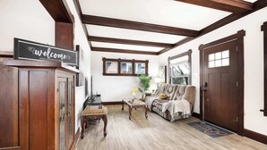 Una sala de estar con piso de madera, un sofá y un tablero de ajedrez, junto con un cartel de bienvenida.