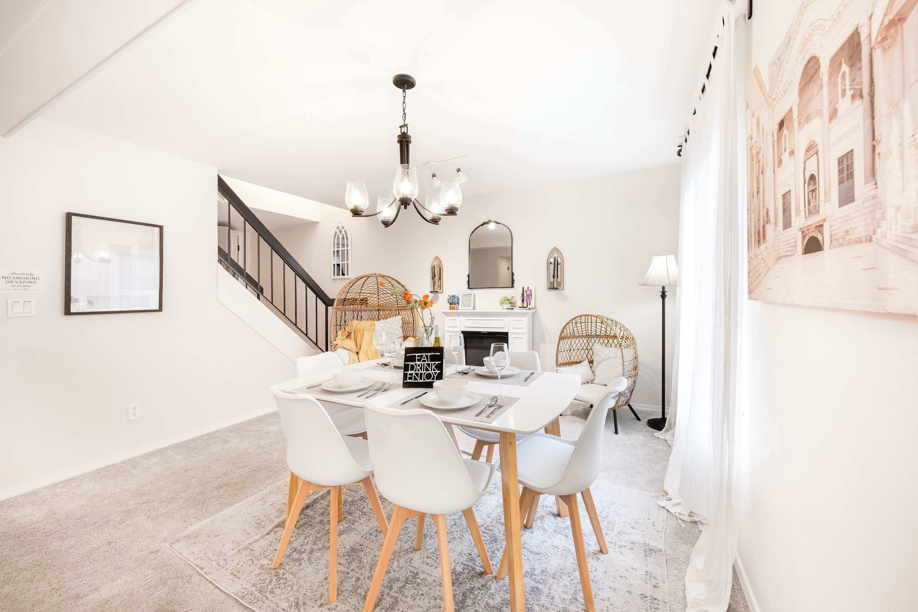 A dining area with a white table set for four, a chandelier, and a staircase leading to an upper level.
