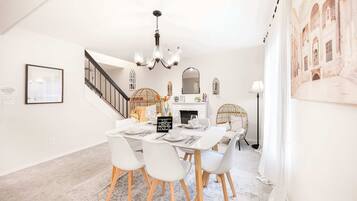 A dining area with a white table set for four, a chandelier, and a staircase leading to an upper level.