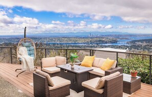 Une terrasse dotée de meubles en osier, d’un fauteuil suspendu et offrant une vue sur la ville et le lac.