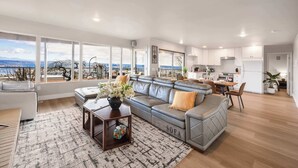 A spacious living area with a grey sofa, a wooden coffee table, and a view of the city through large windows. - Luxury Bellevue 2B Basement w/ 180º+ Stunning View (Bellevue)