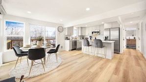A modern kitchen with white cabinets, stainless steel appliances, and a dining area with a white rug and black chairs.
