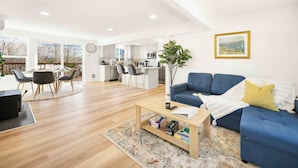 A spacious living room with a blue sofa, a coffee table, and a dining area with chairs and a table.
