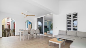Un amplio salón con piso de madera, un sofá gris, una mesa de comedor con sillas y un ventilador de techo.