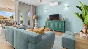 Una sala de estar moderna con sofás color turquesa, un ventilador de techo de madera, un televisor sobre un mueble color turquesa y una planta grande en maceta.