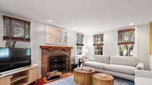 A living room with a fireplace, a television, a sofa, and a coffee table. - Rare Private Deck, Dog Friendly, Walk to Harbor! (Provincetown)