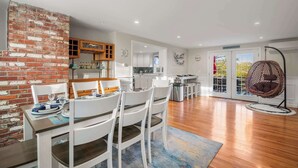 Een moderne keuken met witte kasten, een accentmuur van baksteen, en een eethoek met witte stoelen en een tafel gedekt voor twee personen.