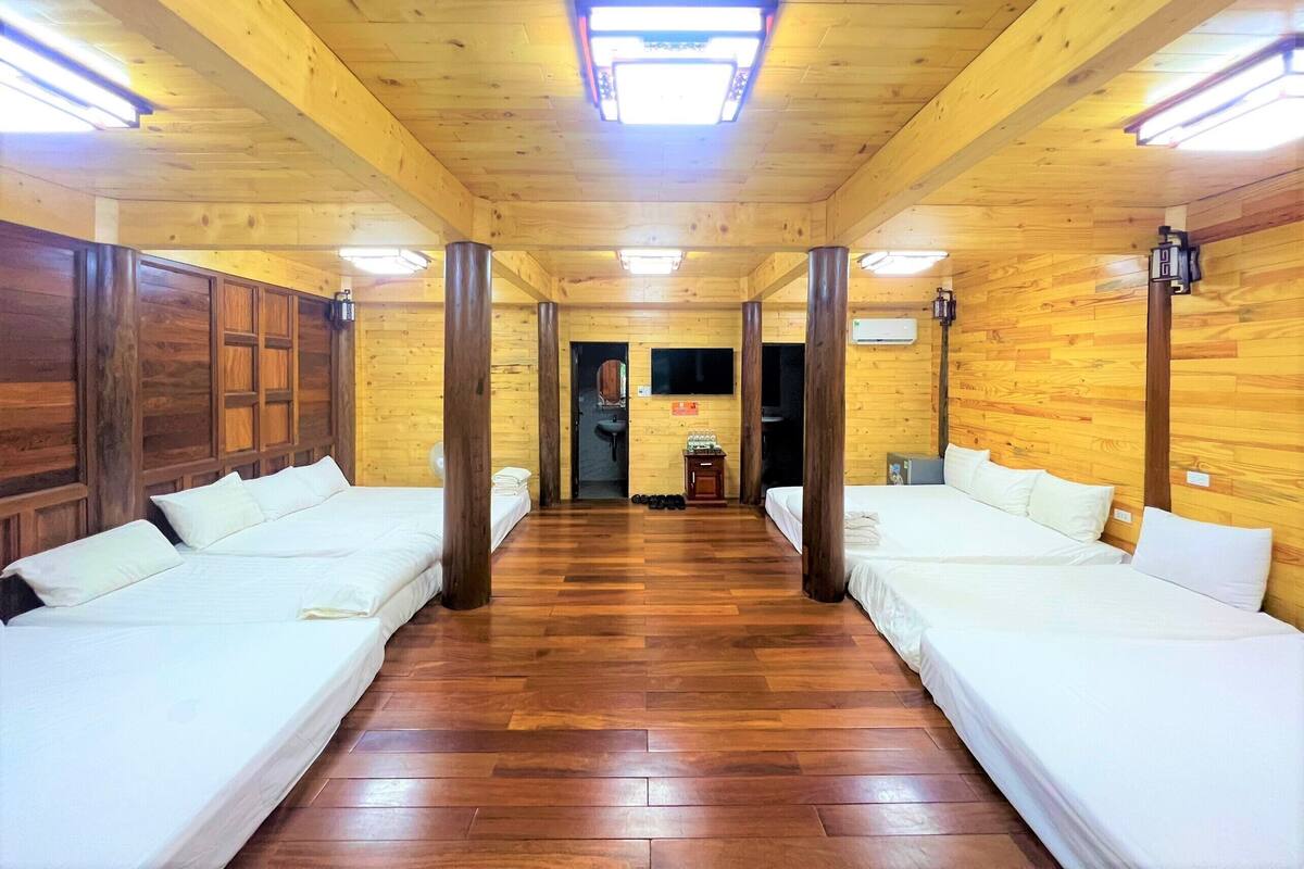 Una habitación con dos camas individuales, paredes y suelo de madera, y un baño pequeño con lavamanos y espejo.