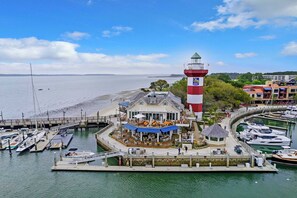A marina with a prominent lighthouse, boats docked, and a waterfront restaurant with outdoor seating.