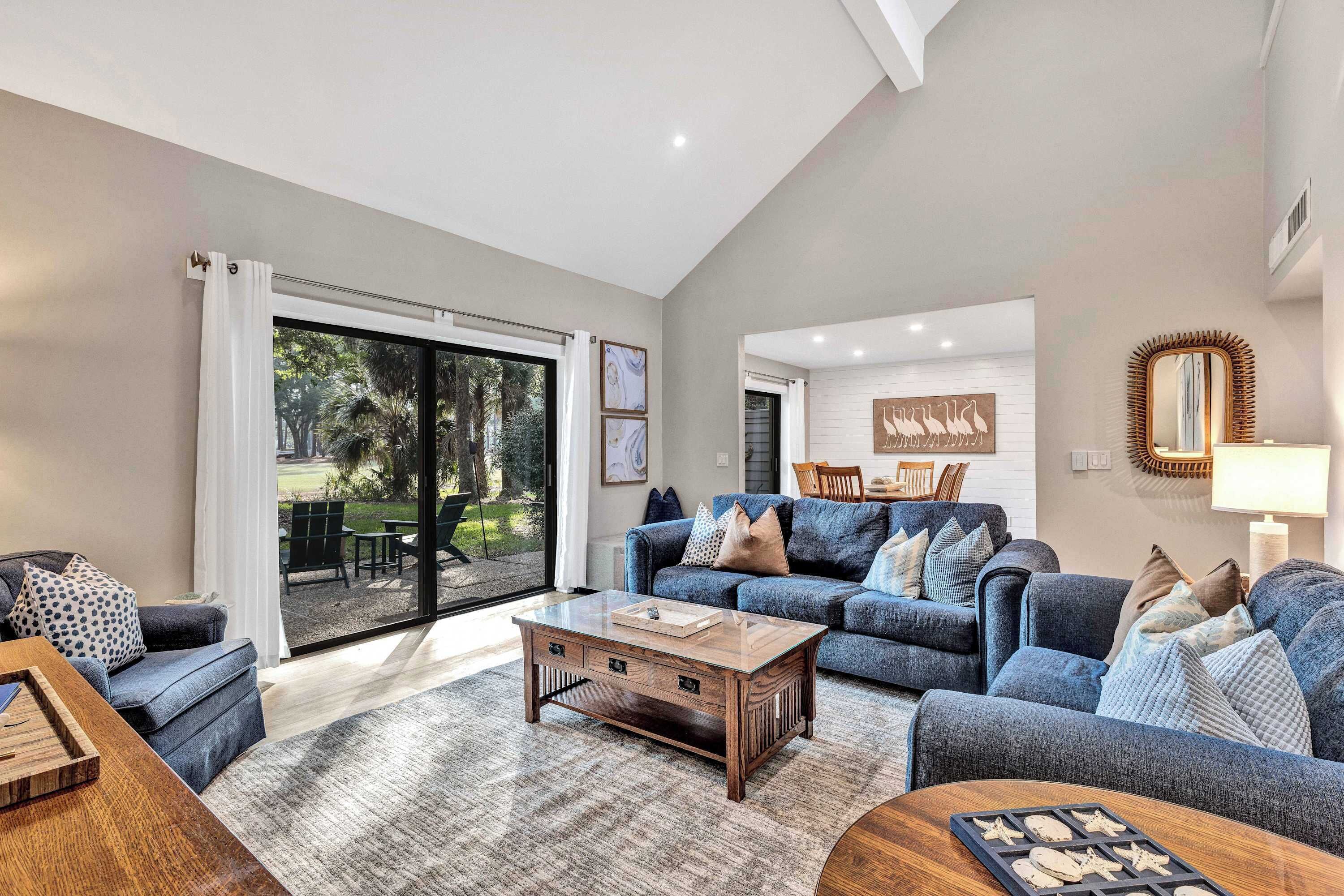 A spacious living room with a large sliding glass door leading to a patio, a blue sofa set, and a wooden coffee table.