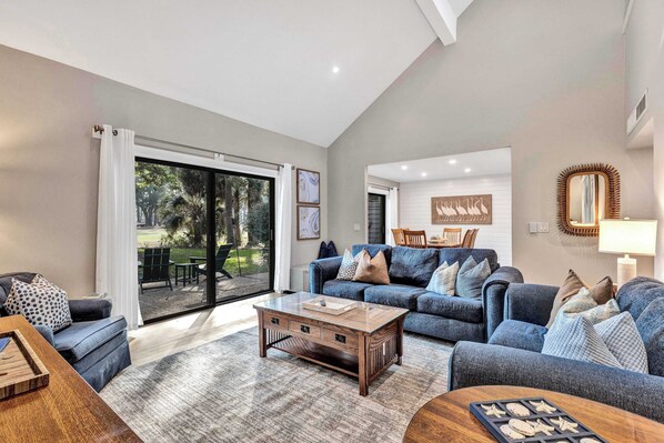 A spacious living room with a large sliding glass door leading to a patio, a blue sofa set, and a wooden coffee table.