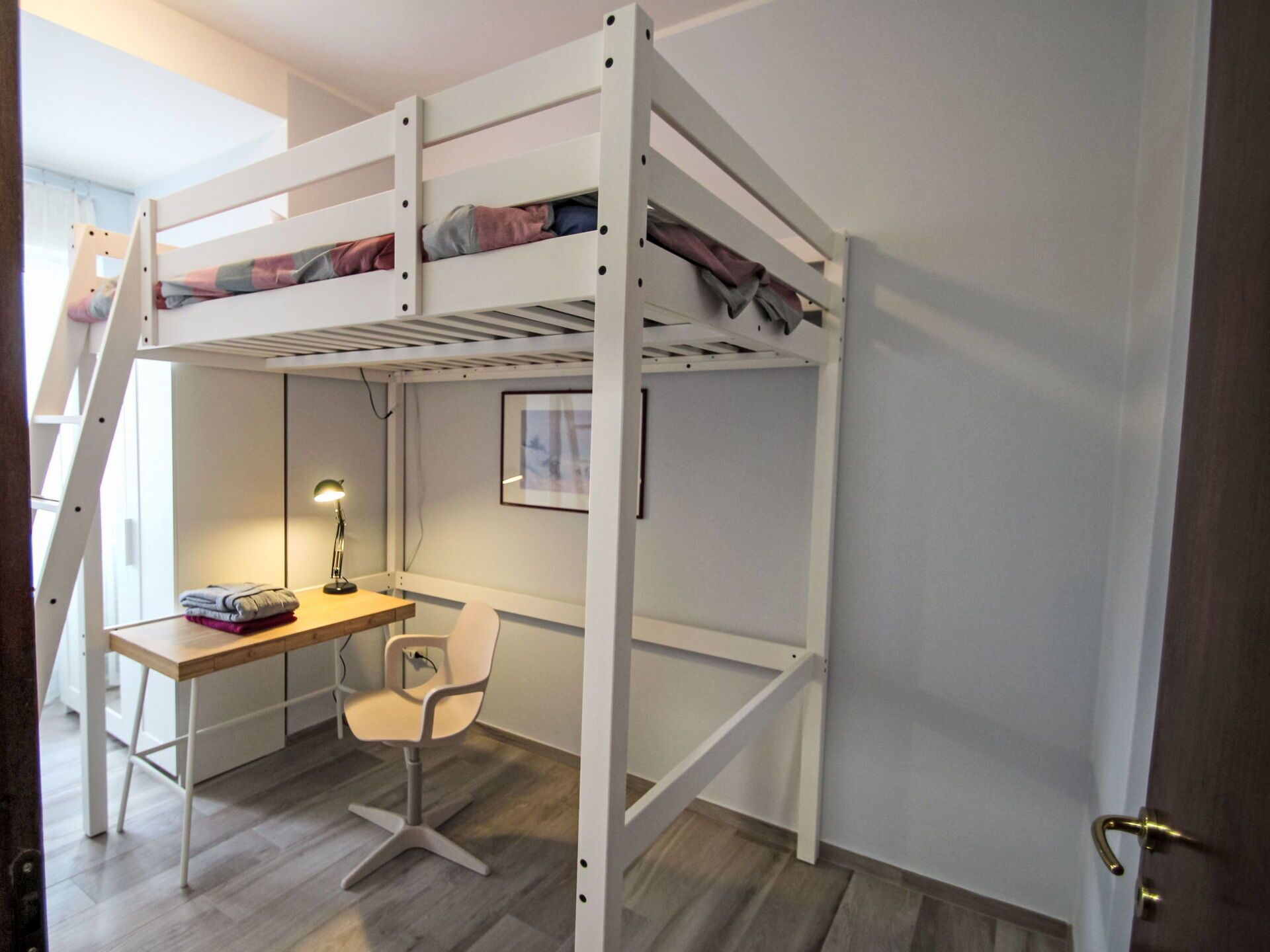 Un lit superposé avec un bureau et une chaise, une lampe et un tableau encadré au mur.