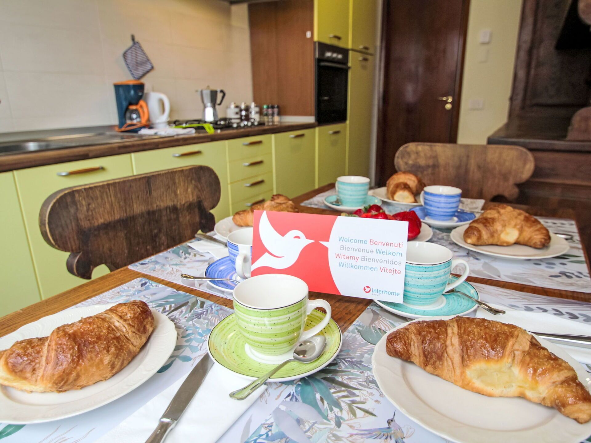 A breakfast setting with croissants, a coffee station, and a welcome sign.