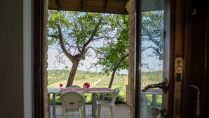 A covered outdoor seating area with a table and chairs, a view of a vineyard, and a door leading into the building. - Lovely apartment for 4 guests with pool, A/C, WIFI, TV, patio and pets allowed (Città Sant'angelo)