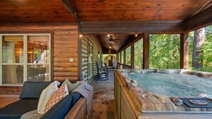 A wooden cabin with a hot tub, a covered porch, and a seating area with cushions.