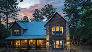 A two-story log cabin with a stone facade, a metal roof, and a porch with a railing.