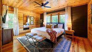 A wooden cabin bedroom with a bed, bench, ceiling fan, and windows.