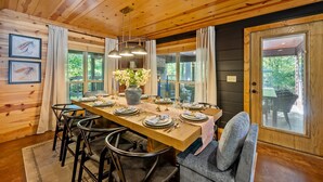 A wooden dining room with a long table set for six, surrounded by chairs.