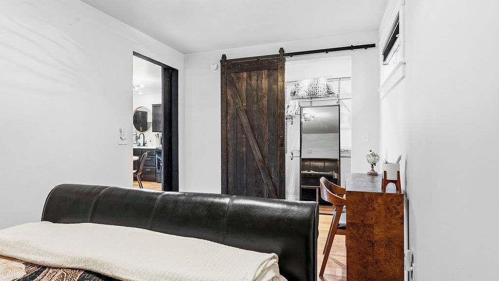 Um quarto com um sofá de couro preto, uma escrivaninha de madeira e uma porta corrediça estilo rústico.