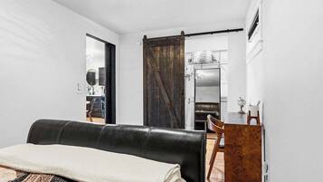 Um quarto com um sofá de couro preto, uma escrivaninha de madeira e uma porta corrediça estilo rústico.