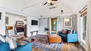 A living room with a blue sofa, a brown ottoman, a patterned rug, and a ceiling fan.