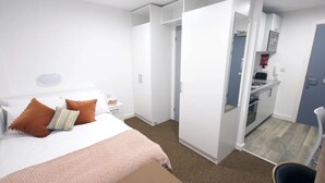 Una camera d'albergo con un letto, un comodino, un armadio e un angolo cottura.