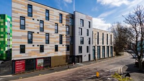 Un edificio moderno con un rivestimento misto di piastrelle beige e verde, diverse finestre e un'insegna con scritto 'The Shield Student Living'.