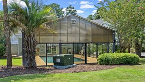 A metal building with a glass enclosure, a pool, and a palm tree. - Sunny Riverwalk Escape | 1BR Condo on the Waterway & Golf Course (Myrtle Beach)