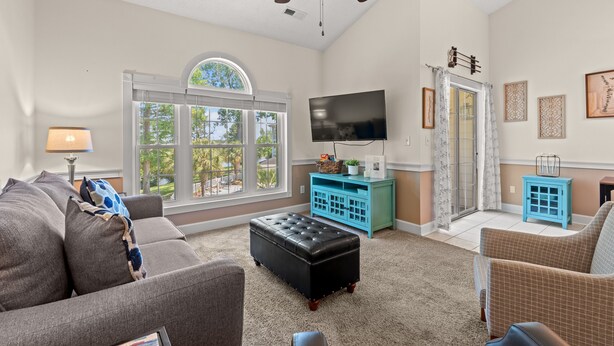 A living room with a sofa, ottoman, and a television on a stand. - Sunny Riverwalk Escape | 1BR Condo on the Waterway & Golf Course (Myrtle Beach)