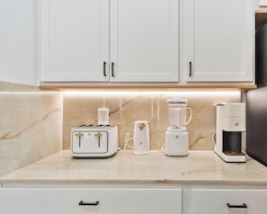 A kitchen with white cabinets, a marble countertop, a toaster, a blender, and a coffee maker.