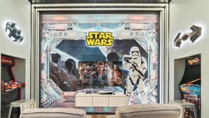 Een kamer met een Star Wars themamuur, speelautomaten en een houten tafel.