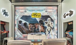 Una habitación con pared temática de Star Wars, juegos de arcade y una mesa de madera.
