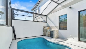A modern outdoor pool area with a built-in grill and a stone accent wall.