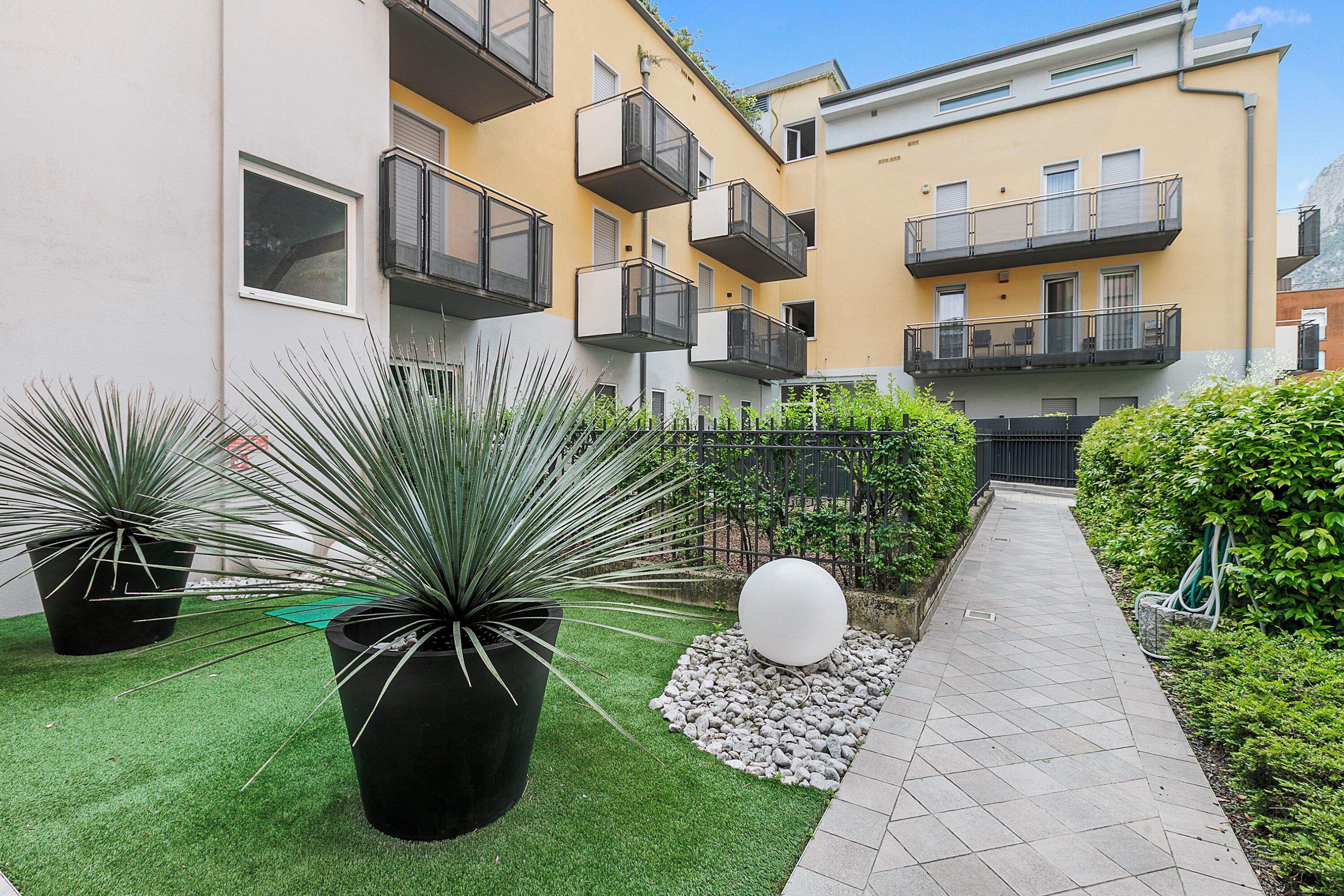 Une cour avec une pelouse artificielle, des plantes en pot, un chemin et un bâtiment doté de balcons.