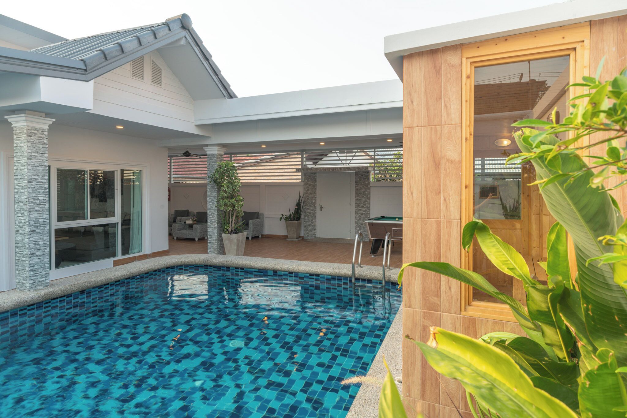 Una casa moderna con piscina, un porche cubierto y una terraza de madera.